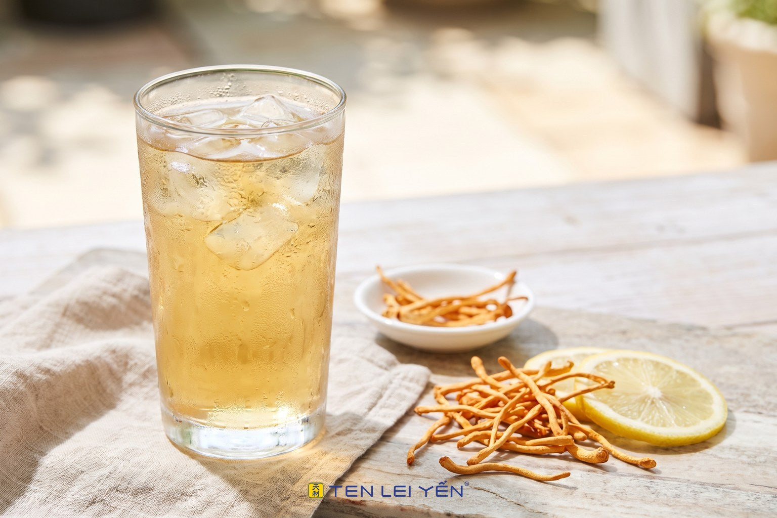 A tall glass of iced cordyceps cooler over ice with a lemon slice and dried cordyceps