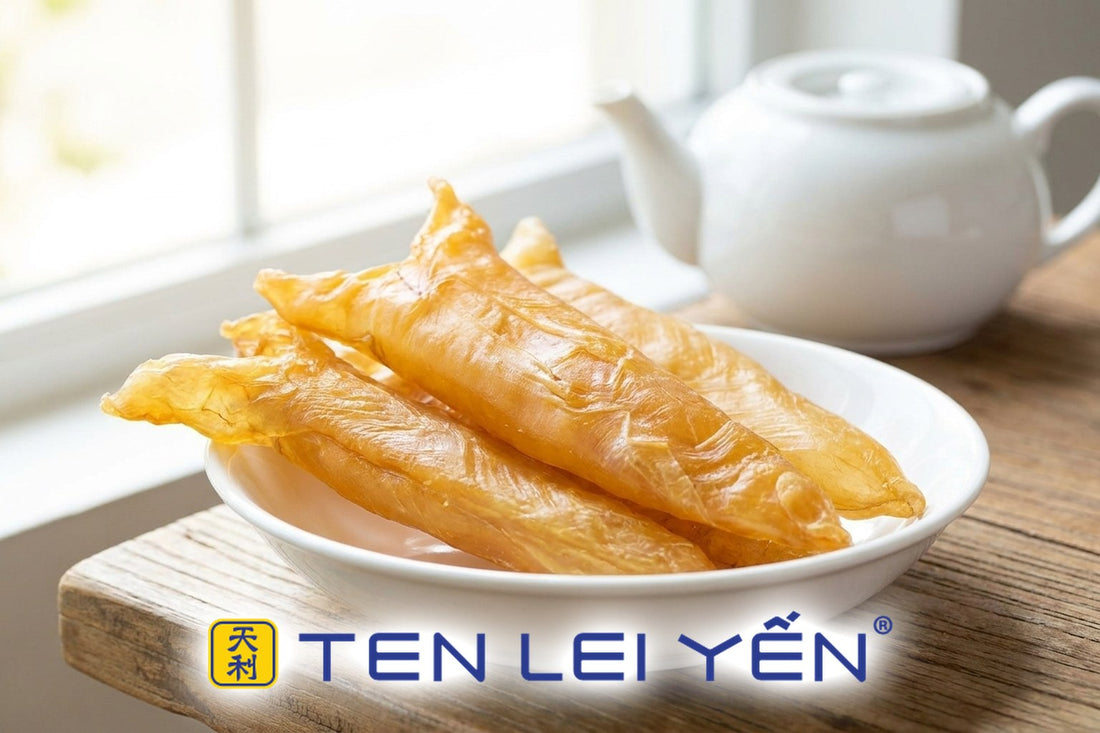 A plate of golden-amber dried fish maw pieces with a smooth, silky longitudinal grain, set on a wooden table near a teapot