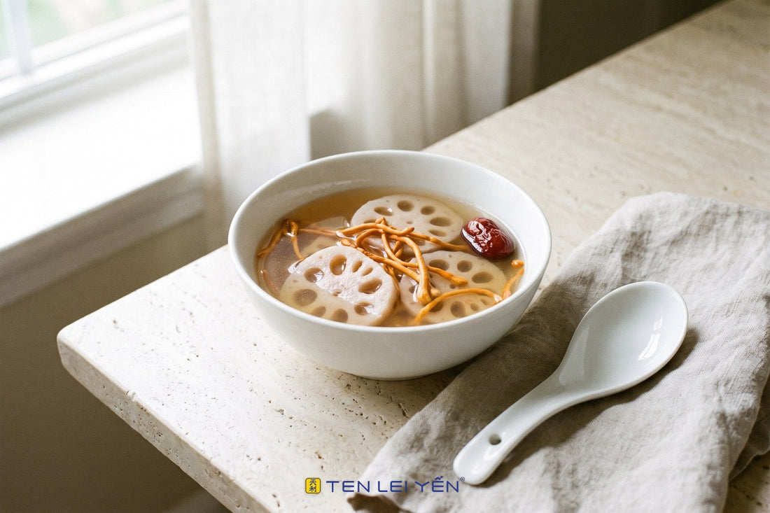 A clear cordyceps and lotus root soup in a white porcelain bowl with round lotus root slices, orange-gold cordyceps stalks, and a red date
