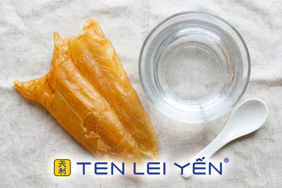 Dried golden-amber fish maw blades resting beside a clear glass bowl of water with a white porcelain spoon