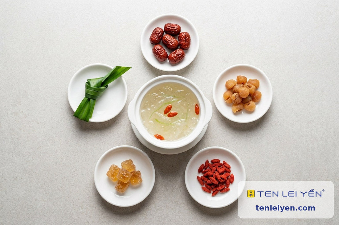 Overhead flat-lay of a bowl of prepared bird's nest surrounded by classic pairings including red dates, longan, goji berries, rock sugar, and pandan leaf